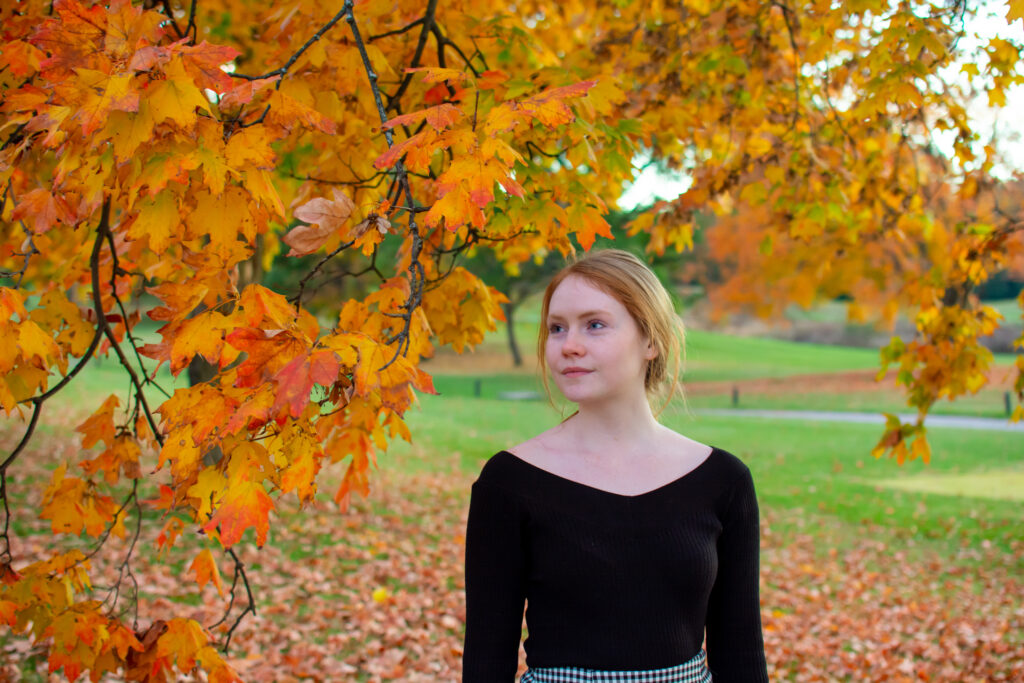 Woman in Autumn, looking to the left surrounded by leaves changing color.