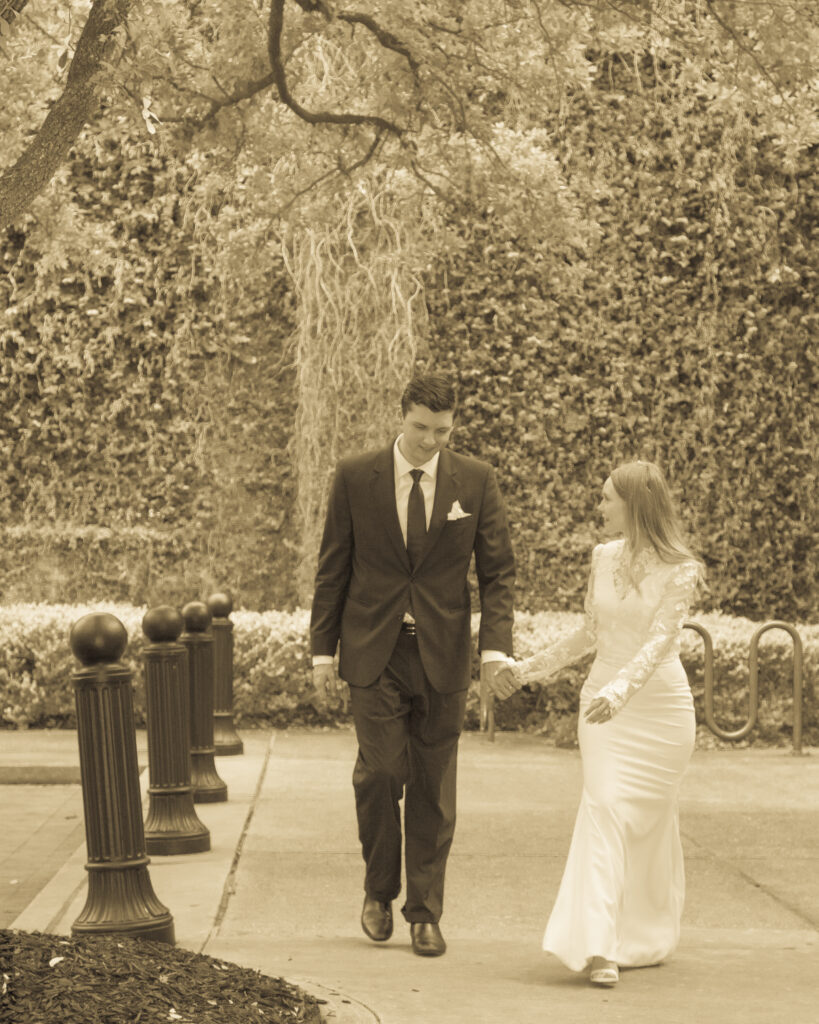 A sepia tone photo of a bride and groom walking and holding each others hands